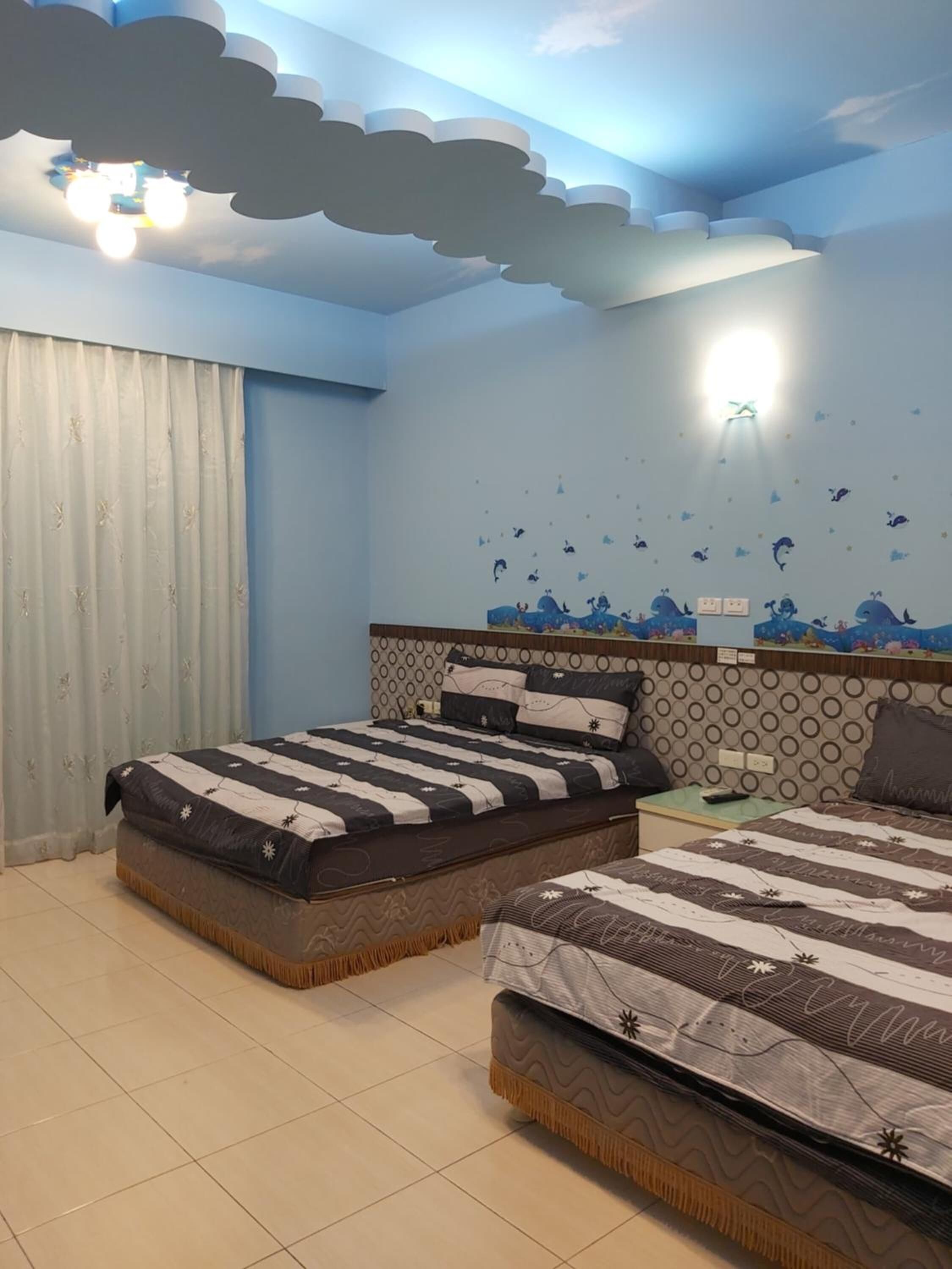 A bedroom with two beds, a ceiling with cloud and star decorations, and a wall with a sea-themed mural.