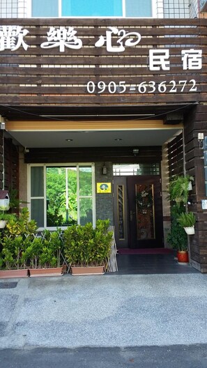 A hotel entrance with a wooden facade, a contact number, and potted plants in the foreground. - Happy Heart B&B (Taitung)