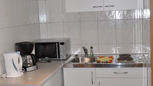 Una cocina pequeña con armarios blancos, un microondas, una cafetera y un lavabo.