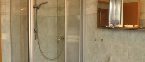 Un baño con ducha envuelta en vidrio, un lavabo y un espejo.