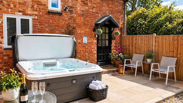 A hot tub in a backyard with a brick house, a wooden fence, outdoor seating, and potted plants. - Juliet Cottage - Sleeps up to 3 - Large Hot Tub (Stratford upon Avon)