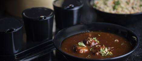 A bowl of meatballs in a dark sauce with a side of rice.