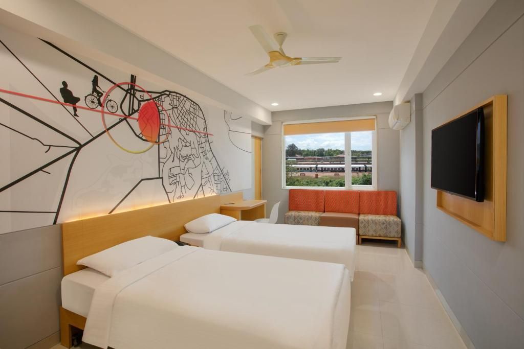 Une chambre d’hôtel avec deux lits, une grande fresque murale, un téléviseur et une fenêtre donnant sur les voies ferrées.