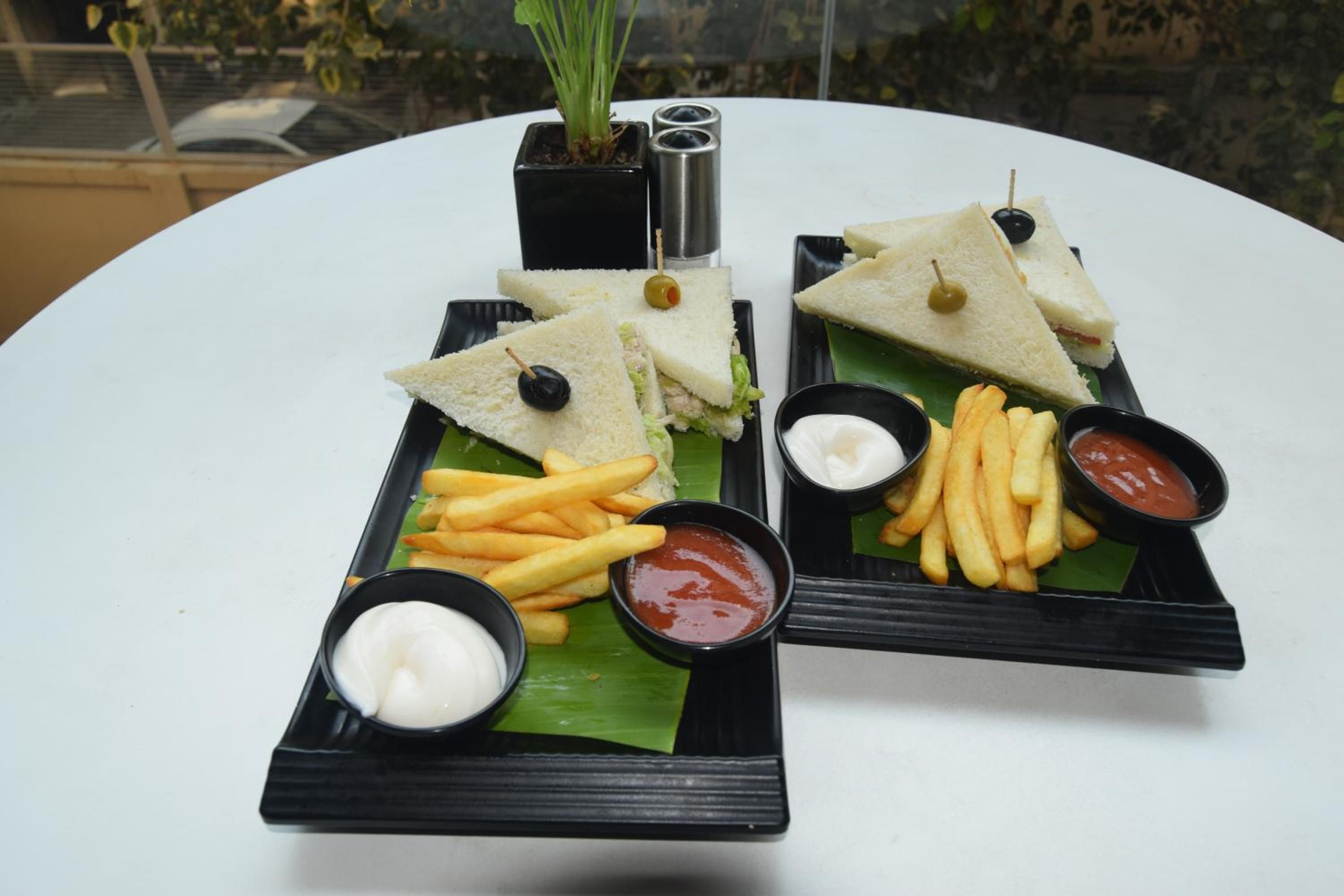 Una mesa con dos platos rectangulares negros que contienen sándwiches, papas fritas y salsas.