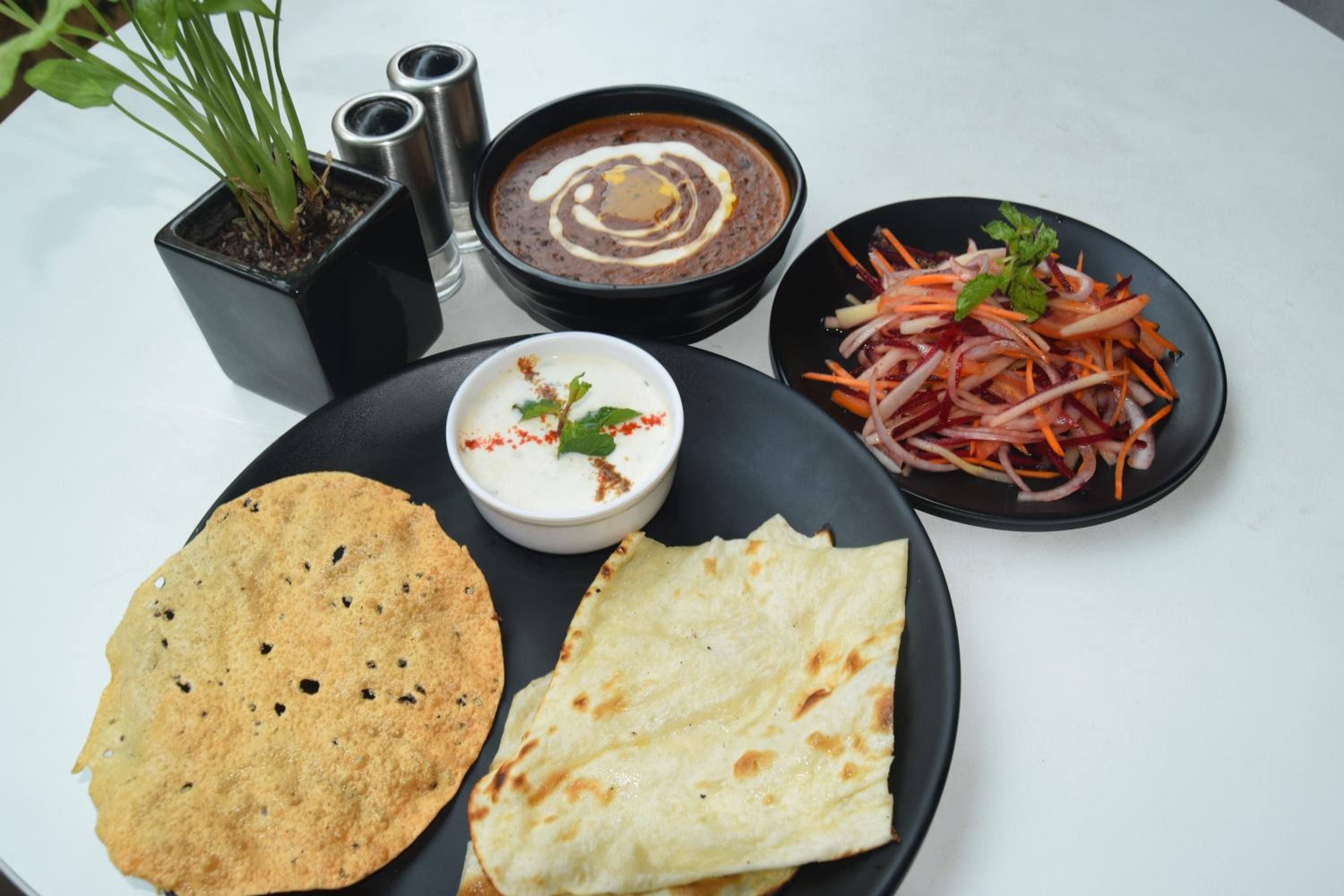 Une table avec un bol de soupe, une assiette de pain plat, une salade et un petit bol de sauce.