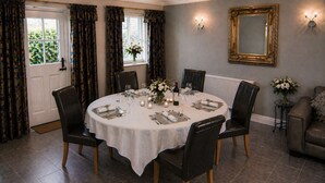 A dining room with a round table set for six, surrounded by chairs, with a vase of flowers and candles on the table.