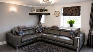 A modern living room with a leather sectional sofa, a dark shag rug, a wall-mounted clock, and a window with a plant.