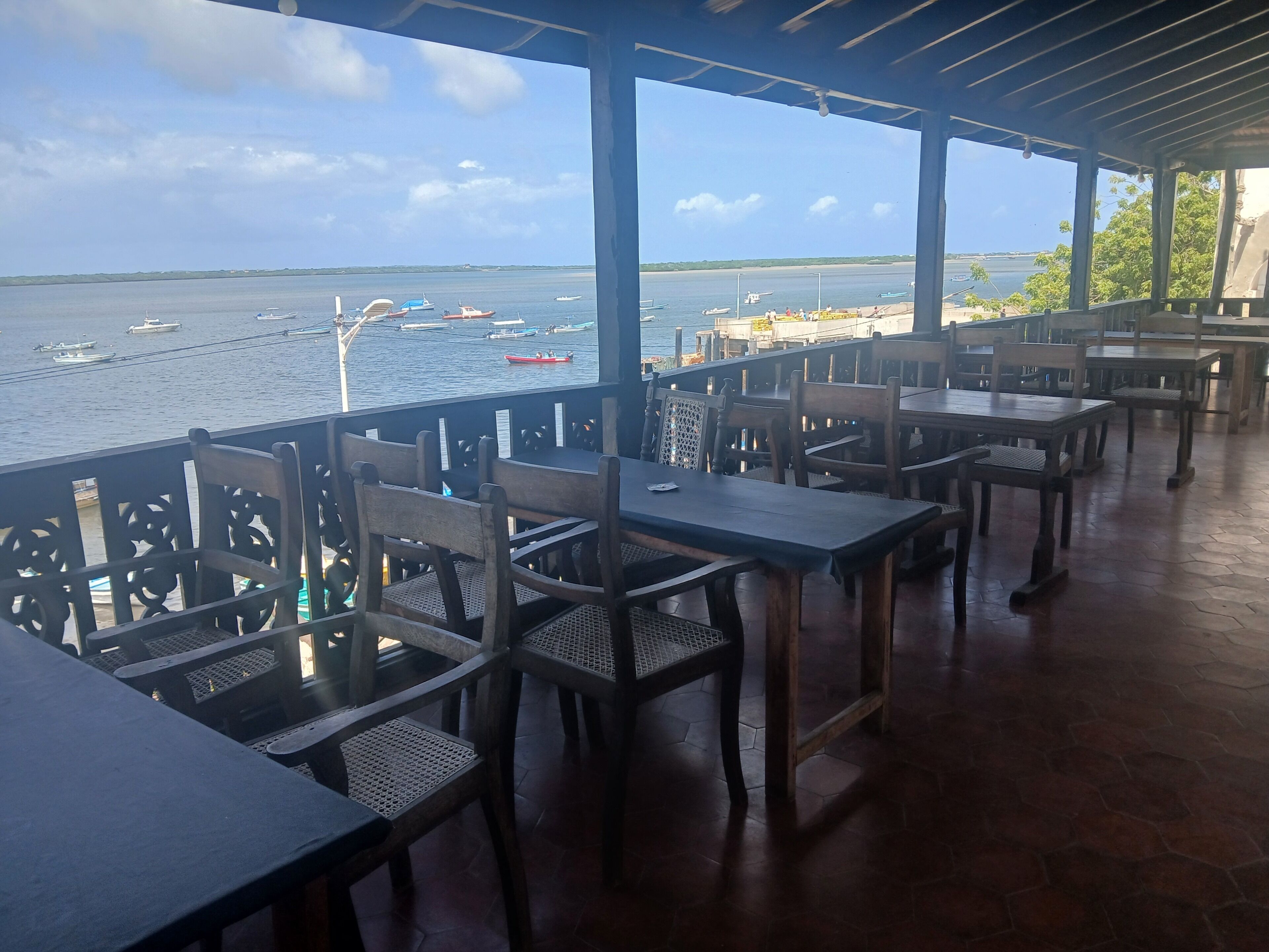 An outdoor dining area with tables and chairs, overlooking a body of water with boats.