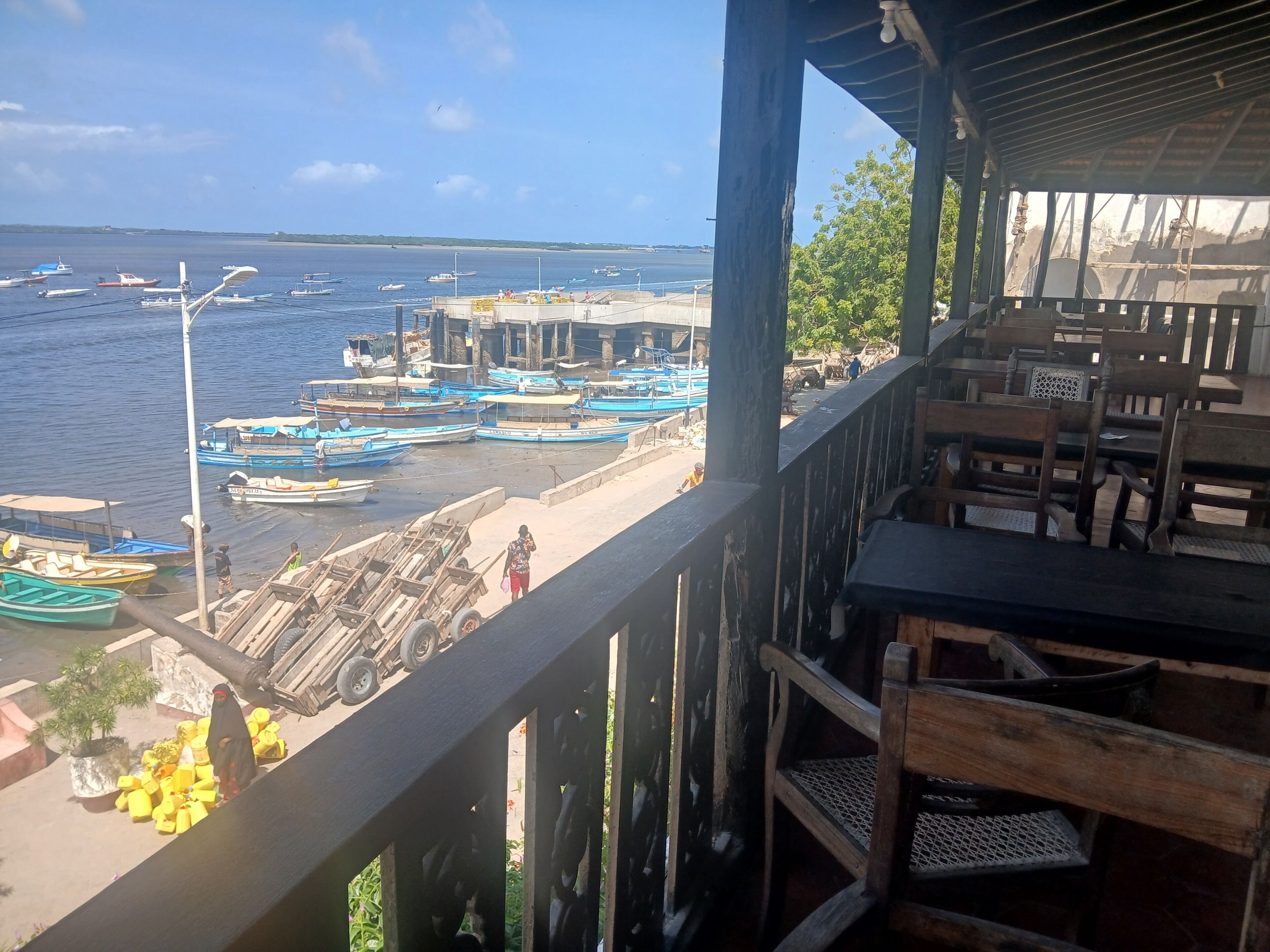 A view from a balcony overlooking a marina with boats docked, a sandy beach, and a building in the background.