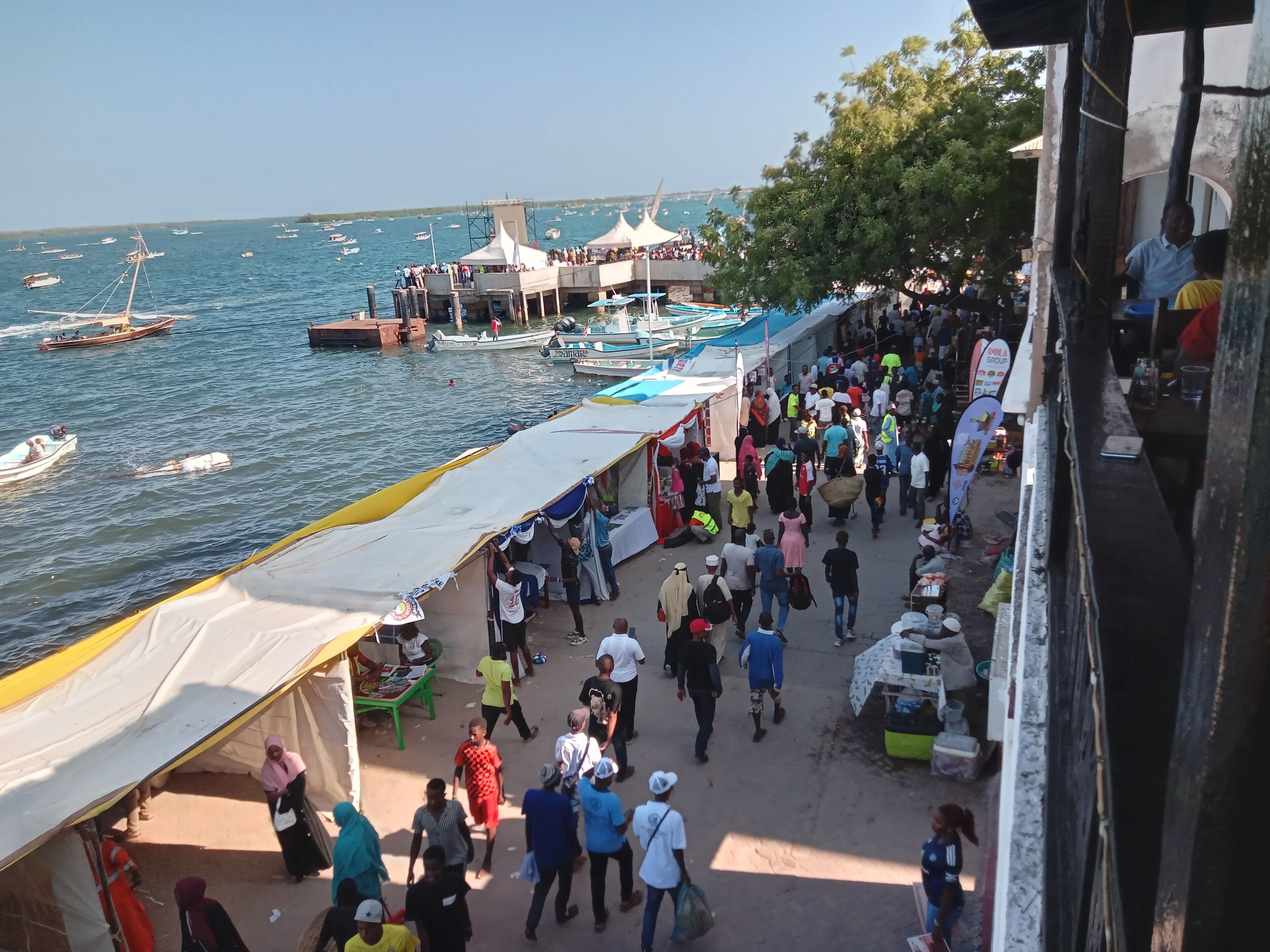 A bustling waterfront market with stalls and people walking along the shore.