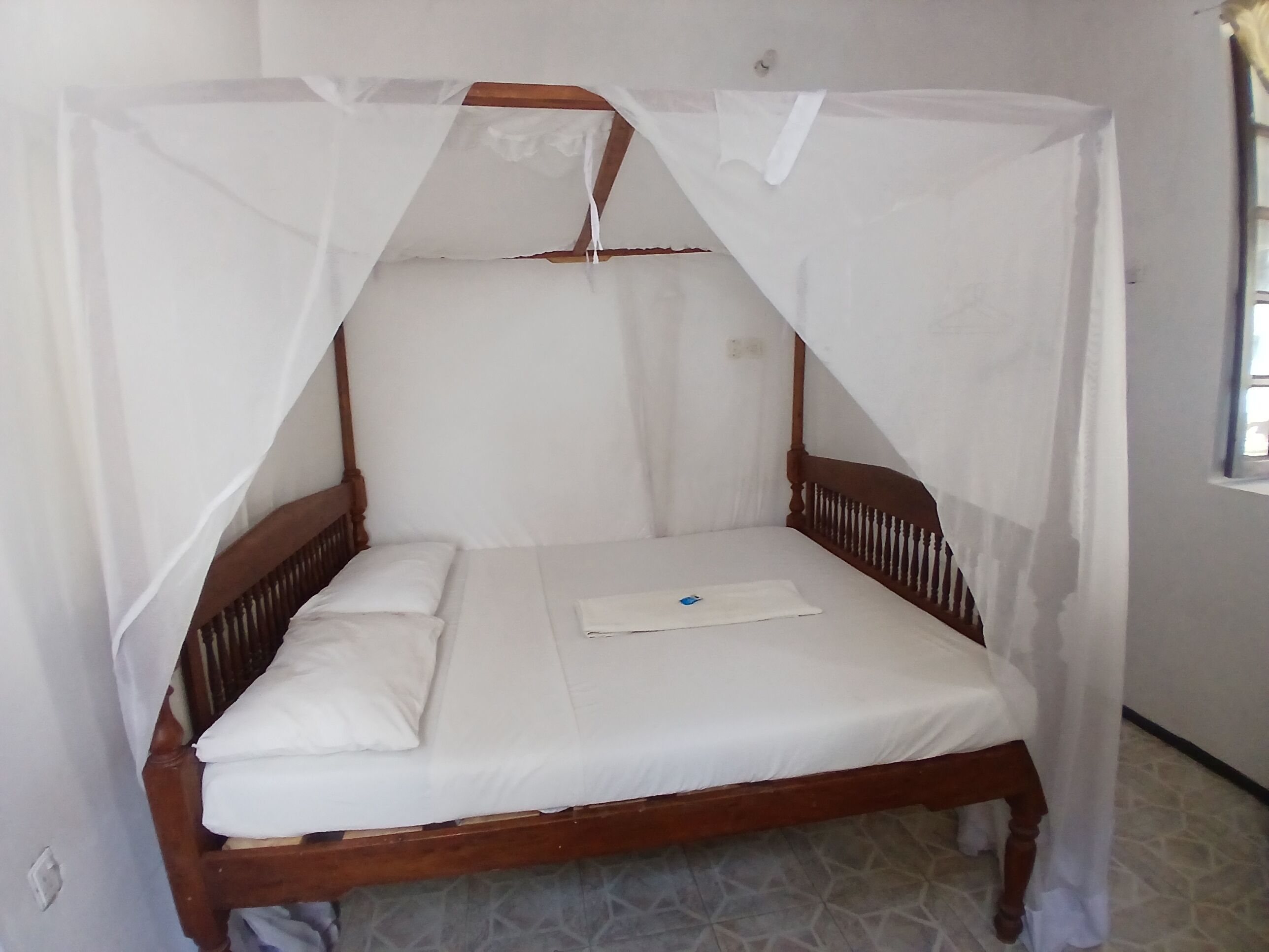 A single bed with a wooden frame and a white mattress, covered by a white canopy.