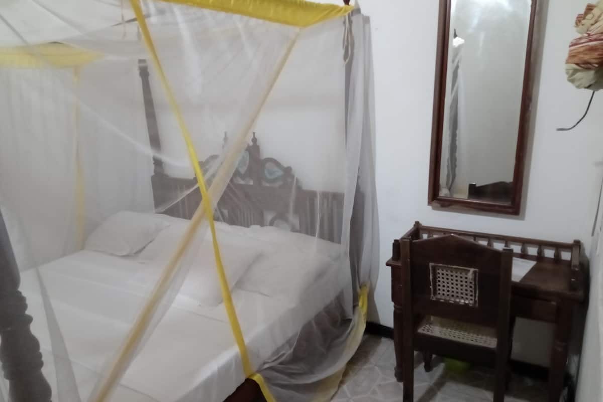 Una cama con dosel, una silla de madera y un espejo en la pared.