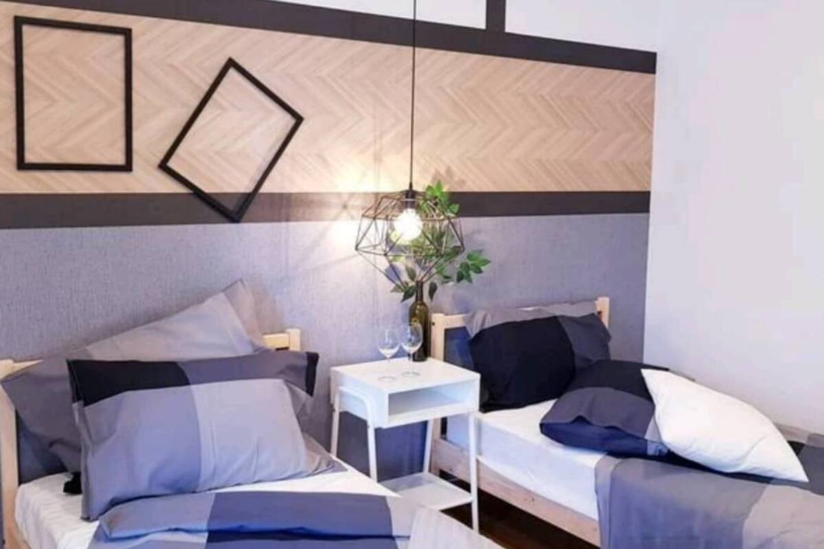 A modern hotel room with two beds, a small white table, and a hanging light fixture.