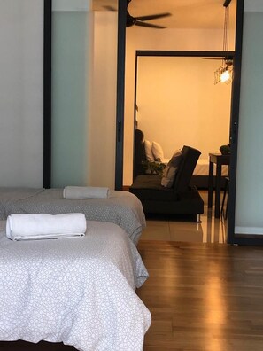 Habitación de hotel con dos camas, ventilador de techo y vista al área de estar contigua.
