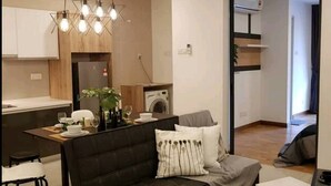 Uma sala de estar moderna com um sofá escuro, uma área de jantar com uma mesa de madeira e uma cozinha ao fundo.