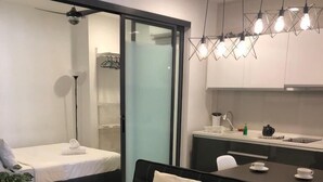Uma sala de estar moderna com um sofá preto, uma mesinha de centro e uma porta de vidro deslizante que dá para um banheiro.