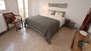 A bedroom with a bed, a chair, a bedside table, a lamp, and a window. - Plaka 2-storey Penthouse with Acropolis views. PL6 (Athens)
