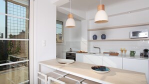 A modern kitchen with white cabinetry, a microwave, and a dining area with a bench. - Plaka 2-storey Penthouse with Acropolis views. PL6 (Athens)