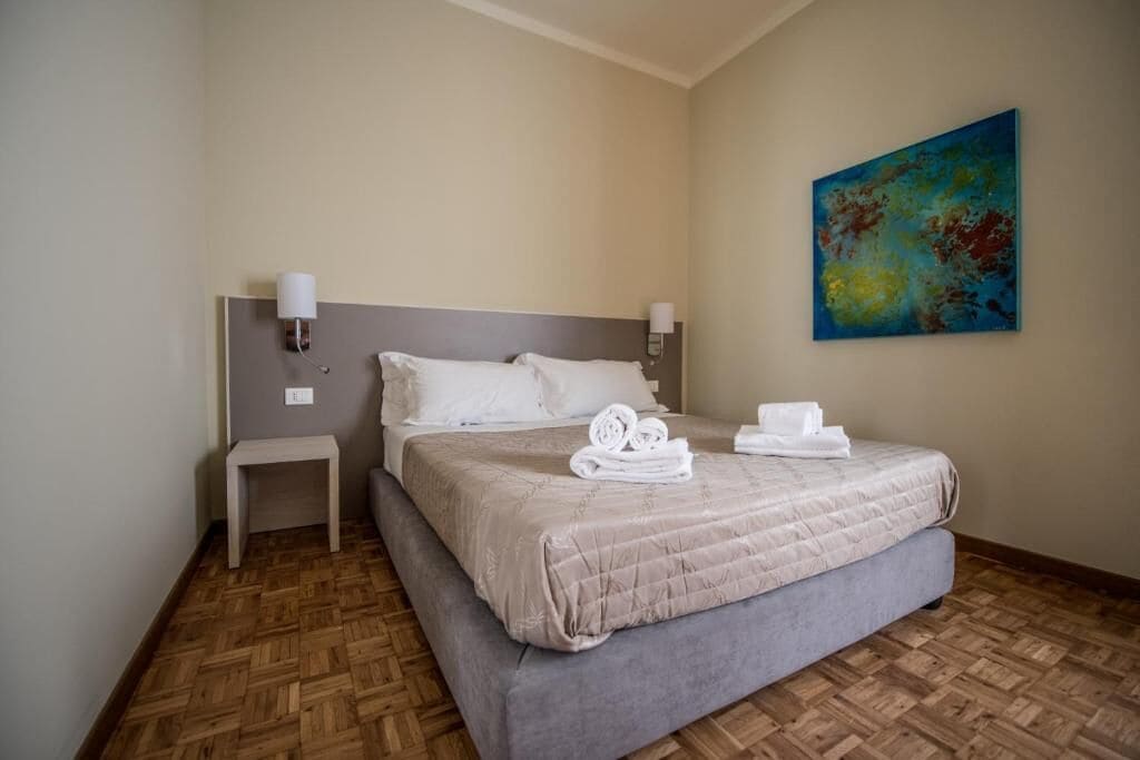 A hotel room with a large bed, a bedside table, and a painting on the wall.