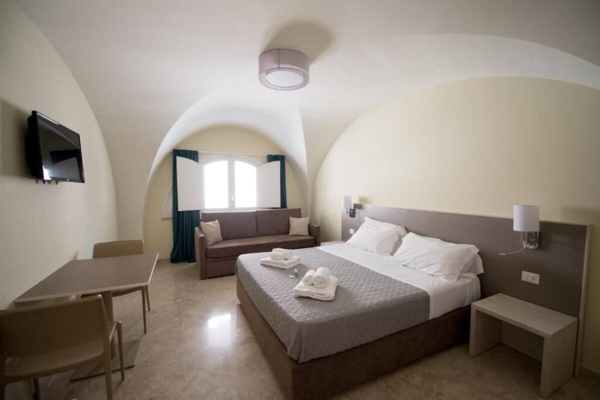 A hotel room with a bed, a desk, a chair, a TV, and a window with curtains.