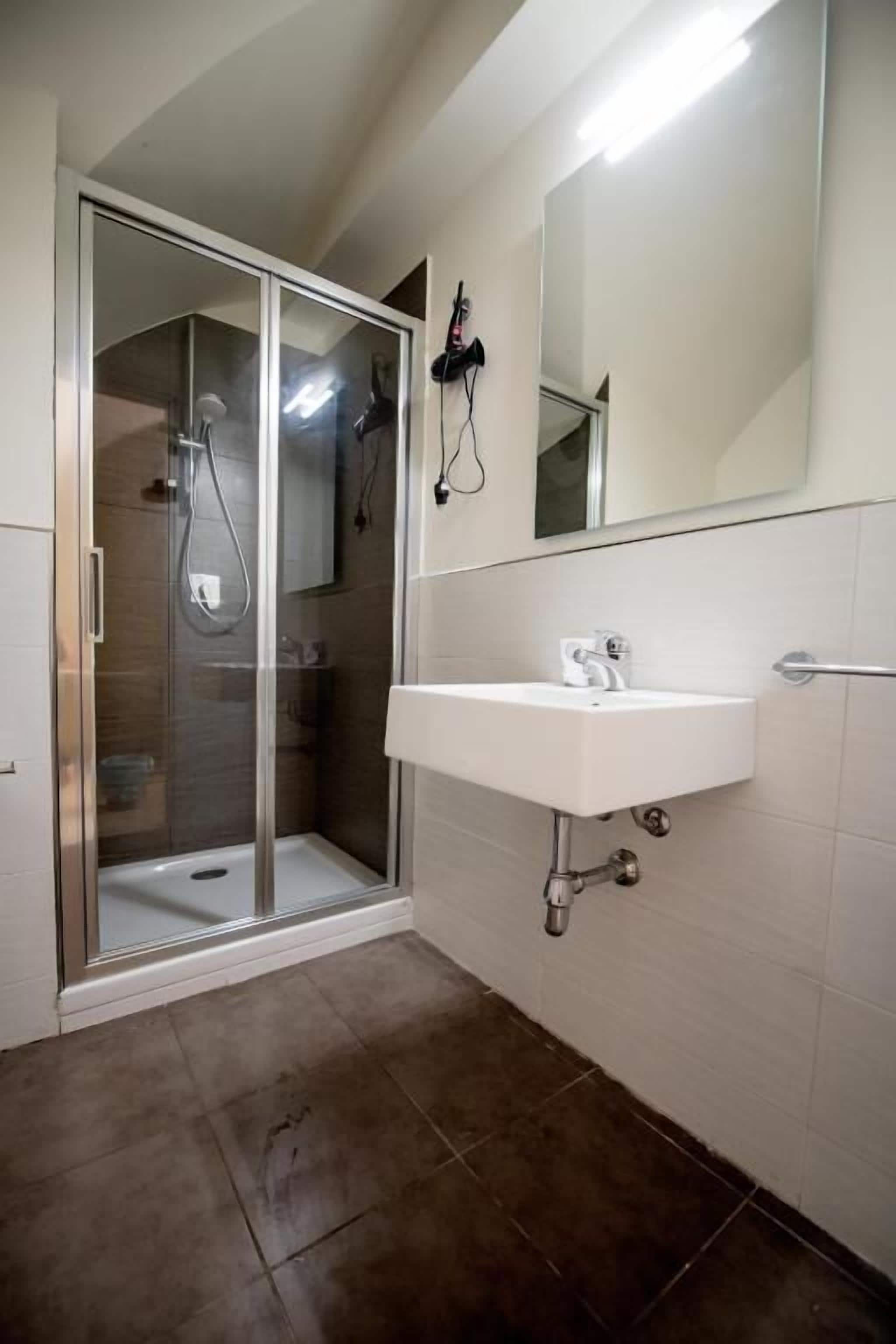 Een moderne badkamer met een douche met glazen wand, een witte wastafel en een grote spiegel.