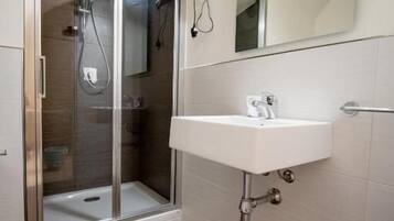 Een moderne badkamer met een douche met glazen wand, een witte wastafel en een grote spiegel.