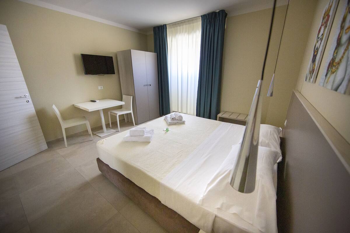 A hotel room with a bed, a desk, a chair, a wardrobe, and a TV on the wall.