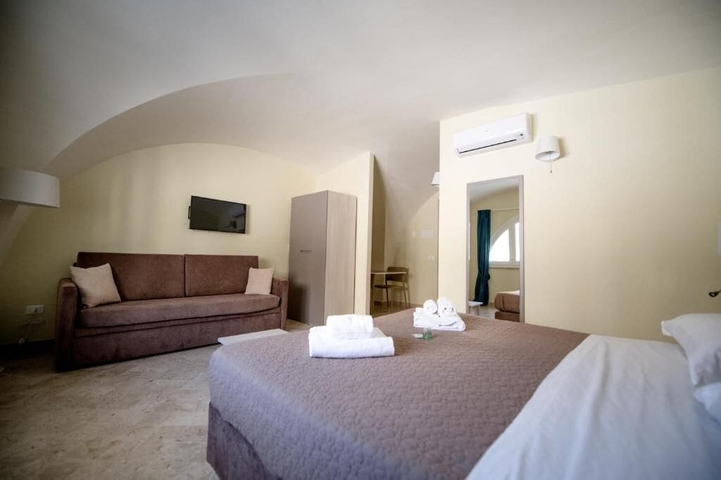 Una habitación de hotel con cama, sofá, armario y aire acondicionado.