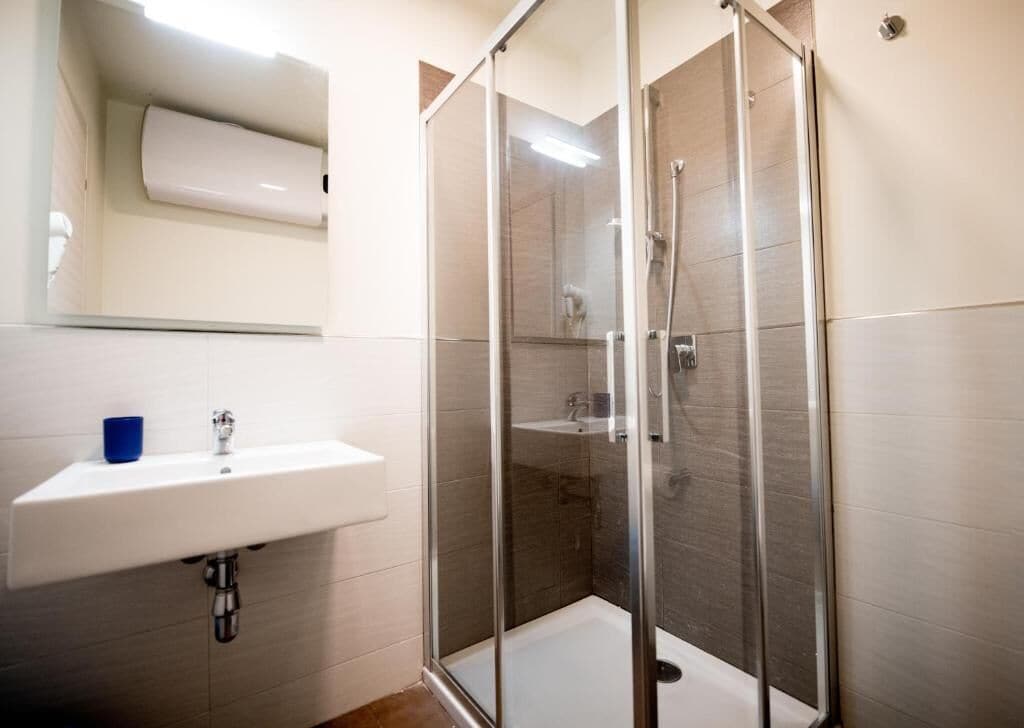 A modern bathroom with a glass-enclosed shower, a white sink, and a mirror above the sink.