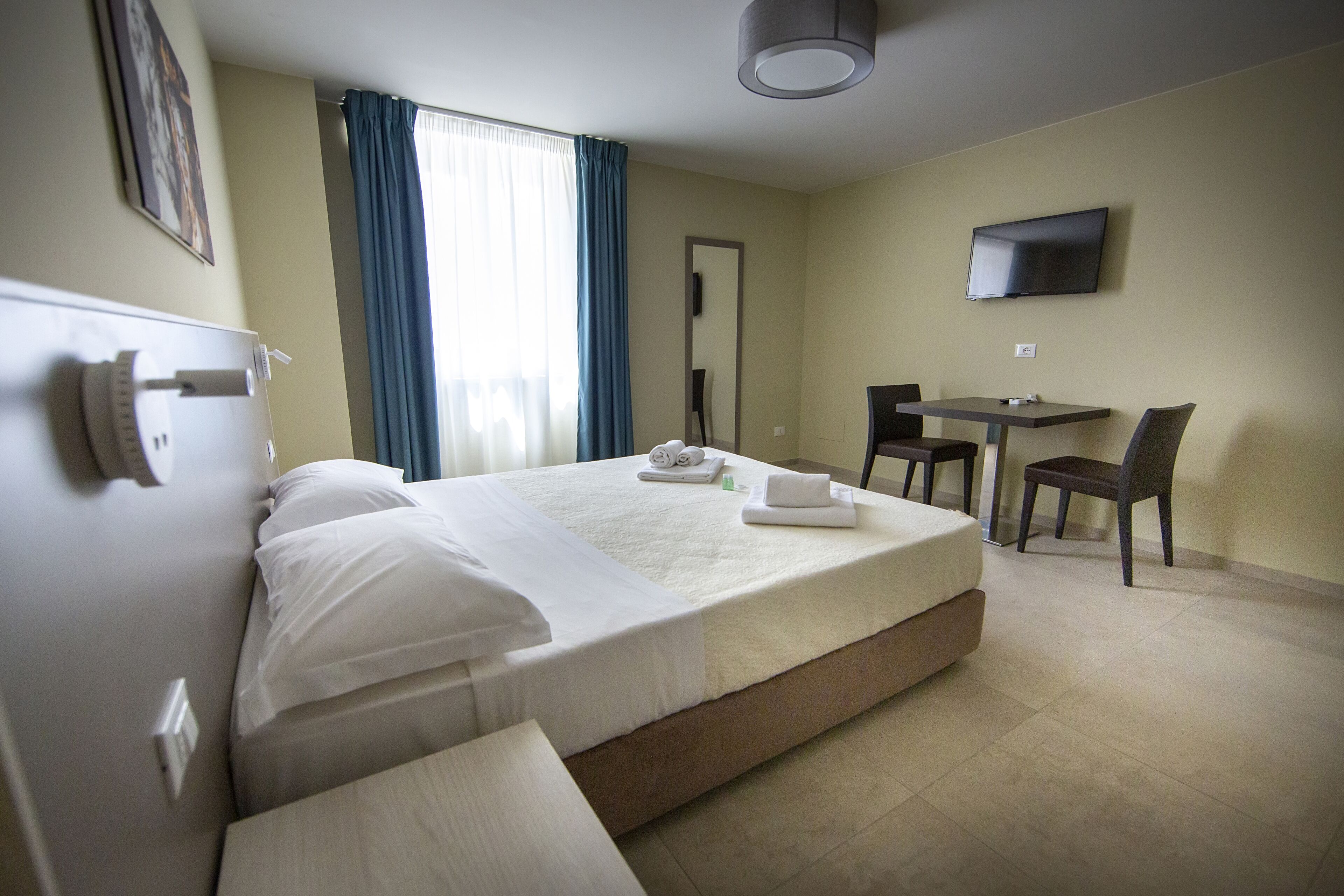 A hotel room with a bed, a desk, a chair, a TV, and a window with curtains.