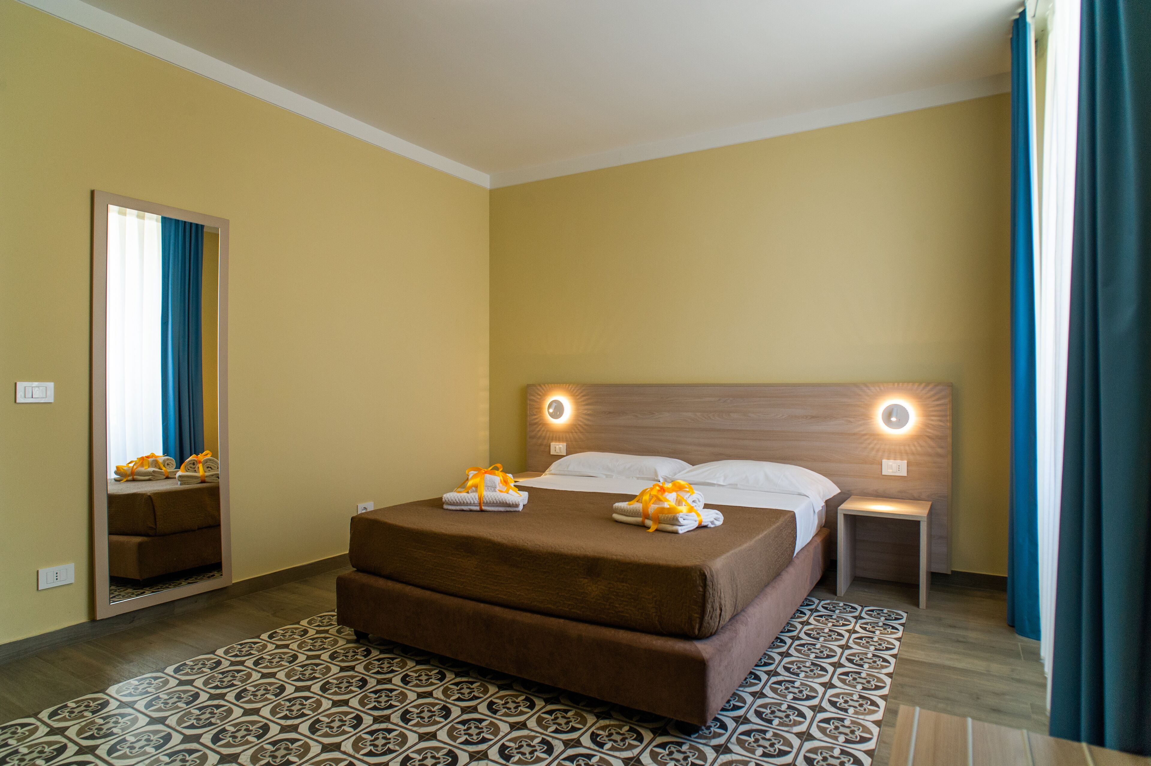 Ein Hotelzimmer mit einem großen Bett, zwei Nachttischen, einem Spiegel und einem gemusterten Teppich.