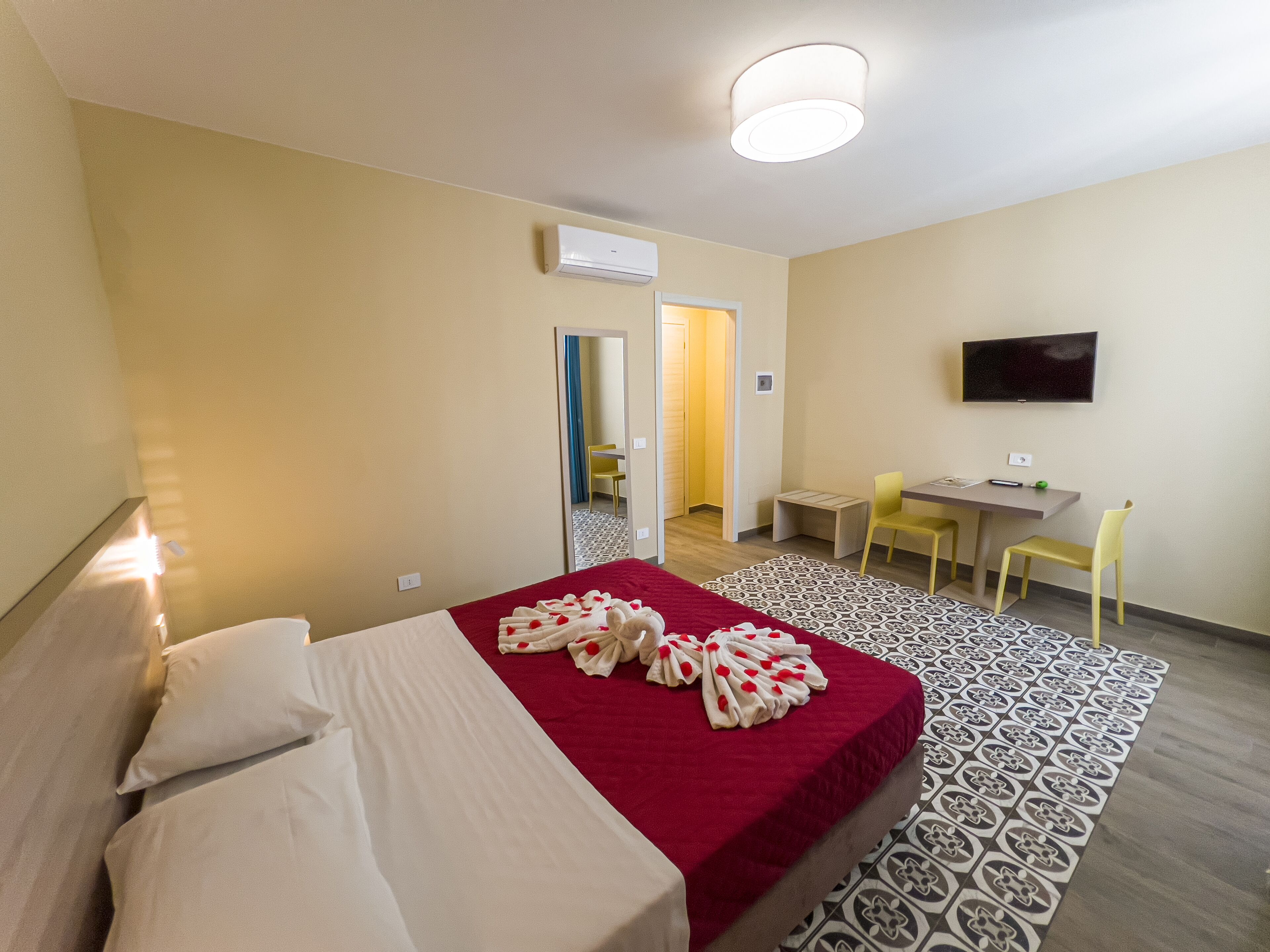 A hotel room with a bed, a desk, a chair, a TV, and a patterned rug.