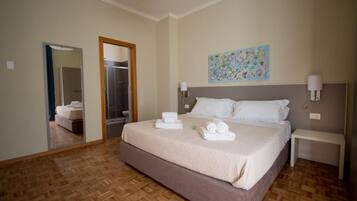 A hotel room with a large bed, a painting on the wall, and a mirror reflecting the room.