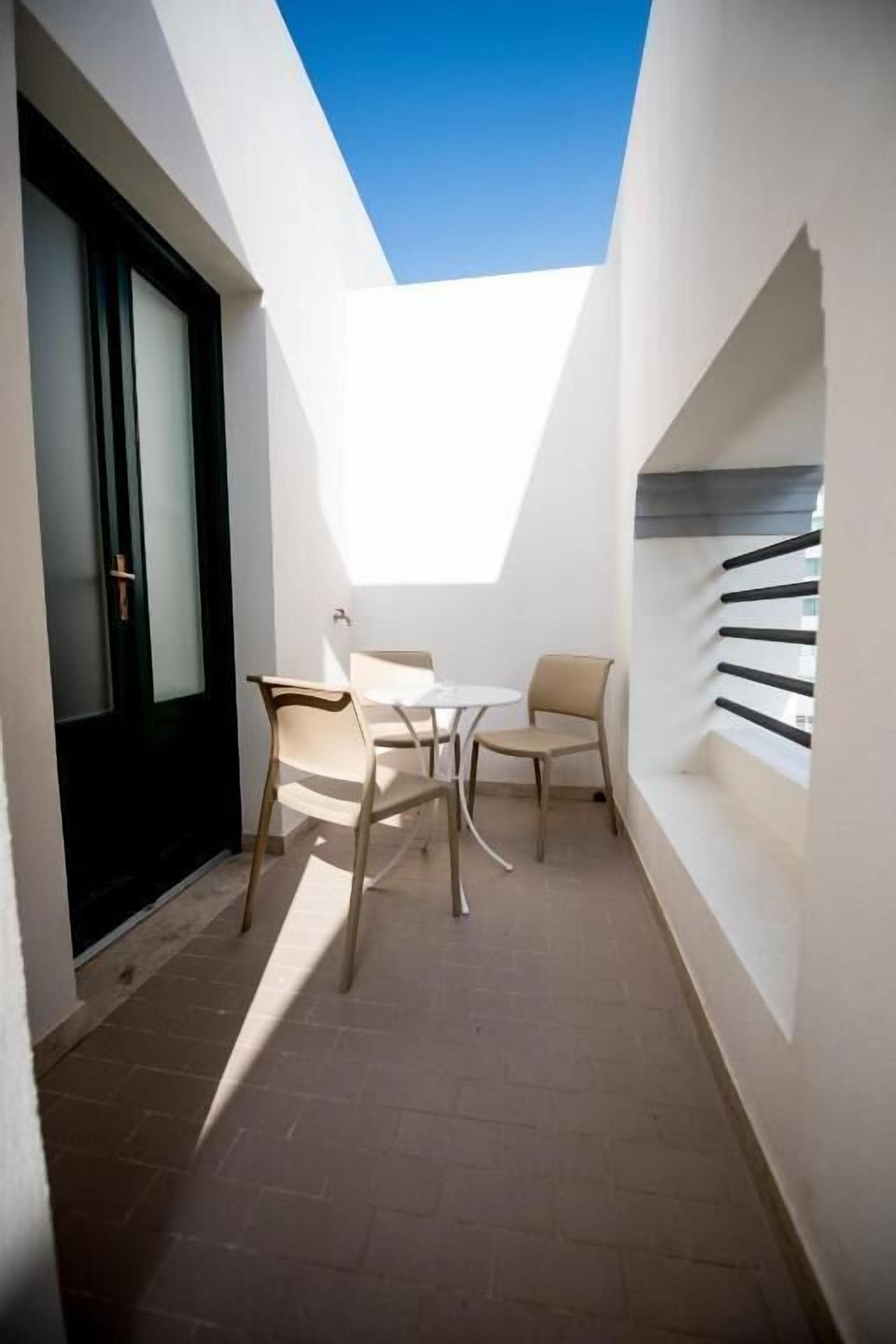 A narrow outdoor space with a table and chairs, a door, and a staircase.