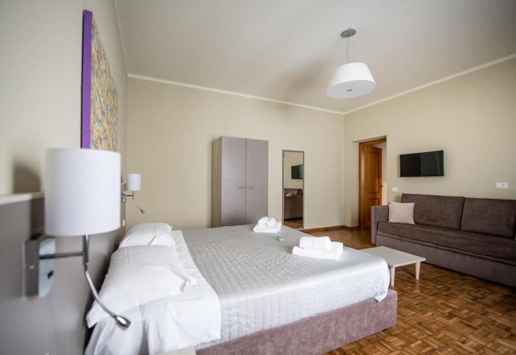 A hotel room with a bed, a sofa, a TV, and a mirror.