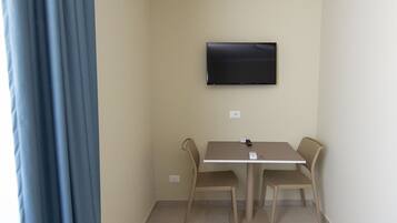 Una habitación pequeña con una mesa, dos sillas, un televisor de pantalla plana en la pared y una cortina a la izquierda.