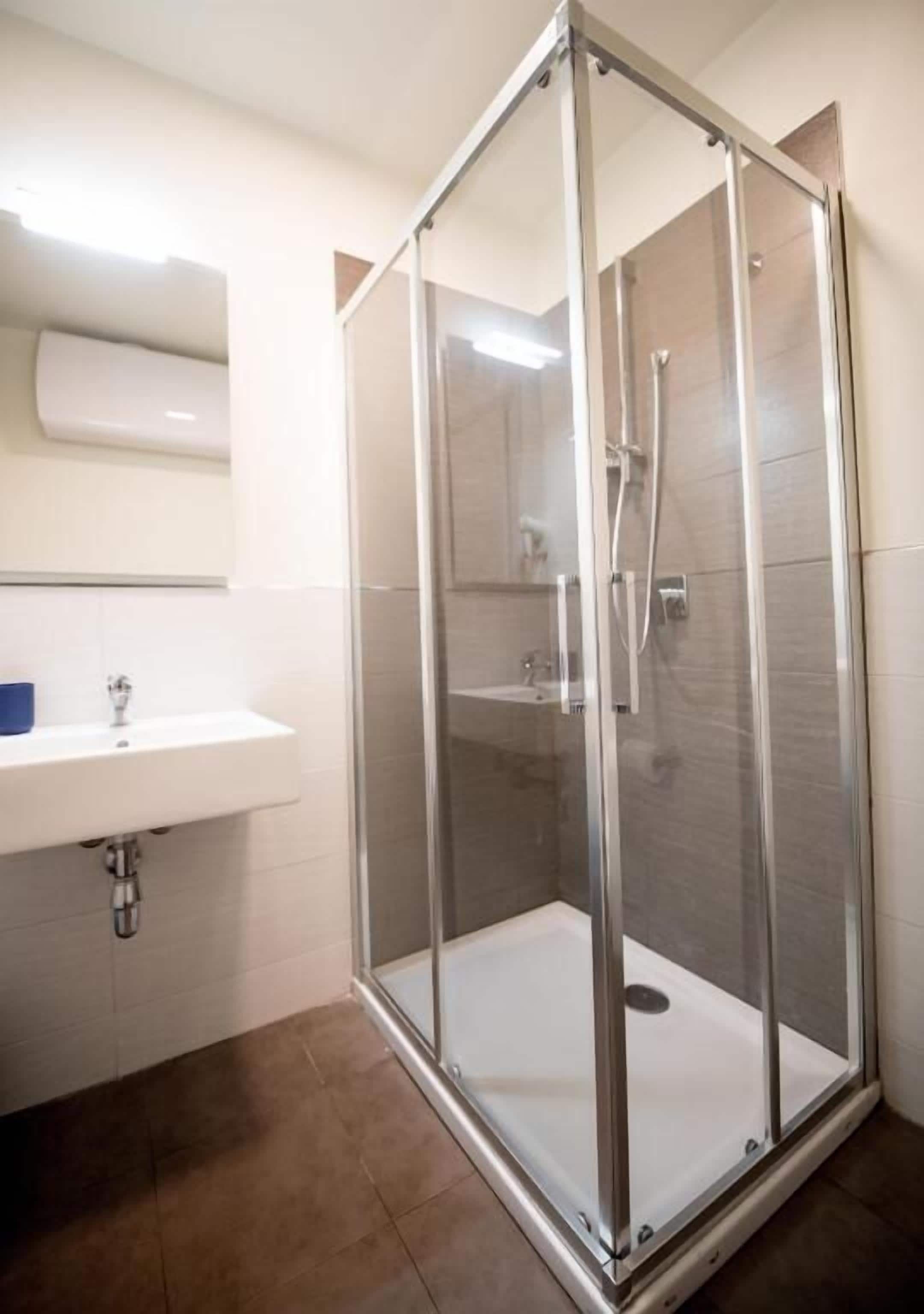 Un baño moderno con ducha de vidrio, un lavamanos blanco y un espejo sobre él.