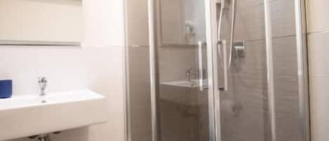 Un baño moderno con ducha de vidrio, un lavamanos blanco y un espejo sobre él.