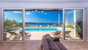 Ein modernes Wohnzimmer mit einem großen Schiebeglastür, die zu einem Poolbereich mit Liegestühlen und Meerblick führt.