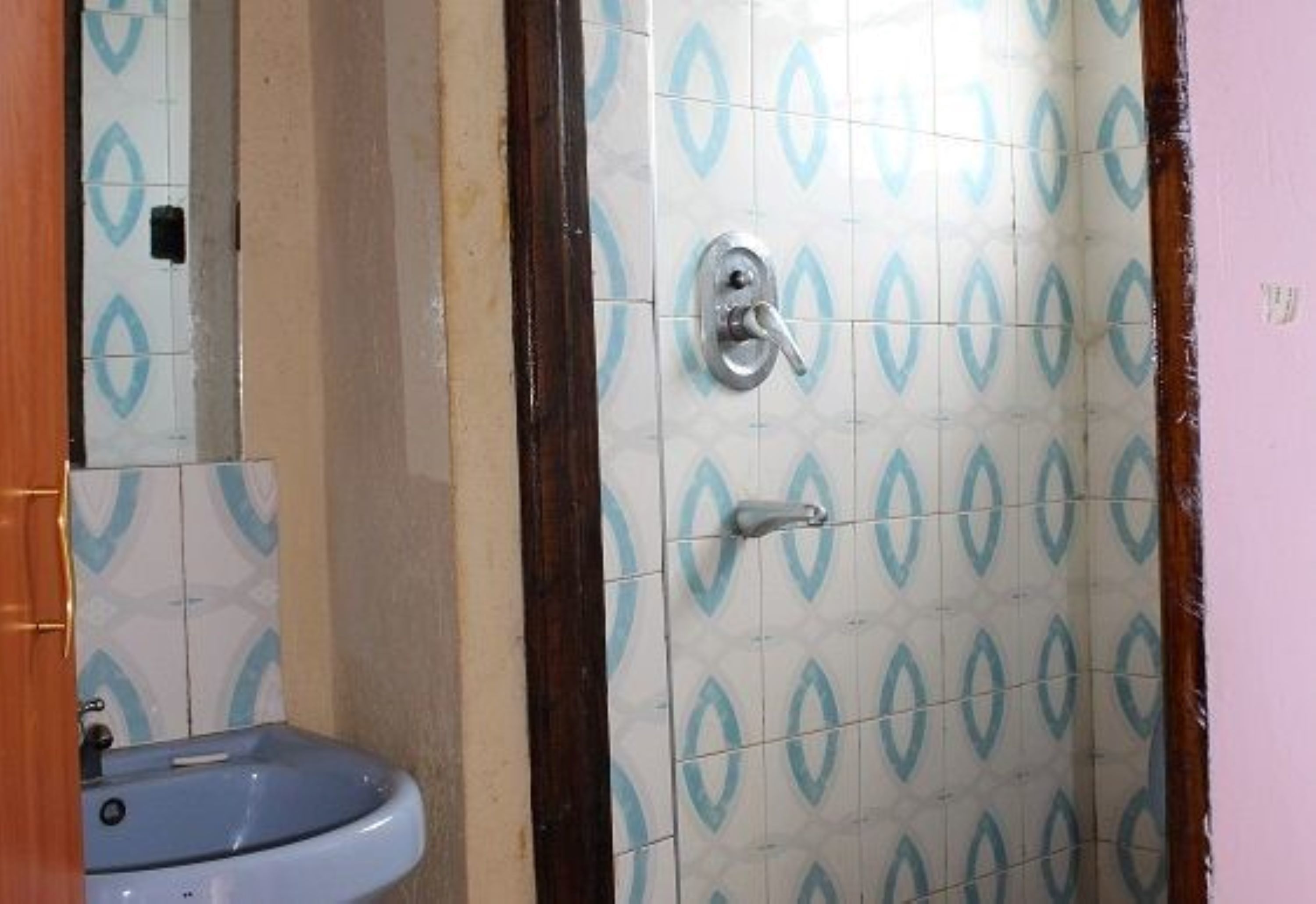 A bathroom with a sink, mirror, and shower area with patterned tiles.
