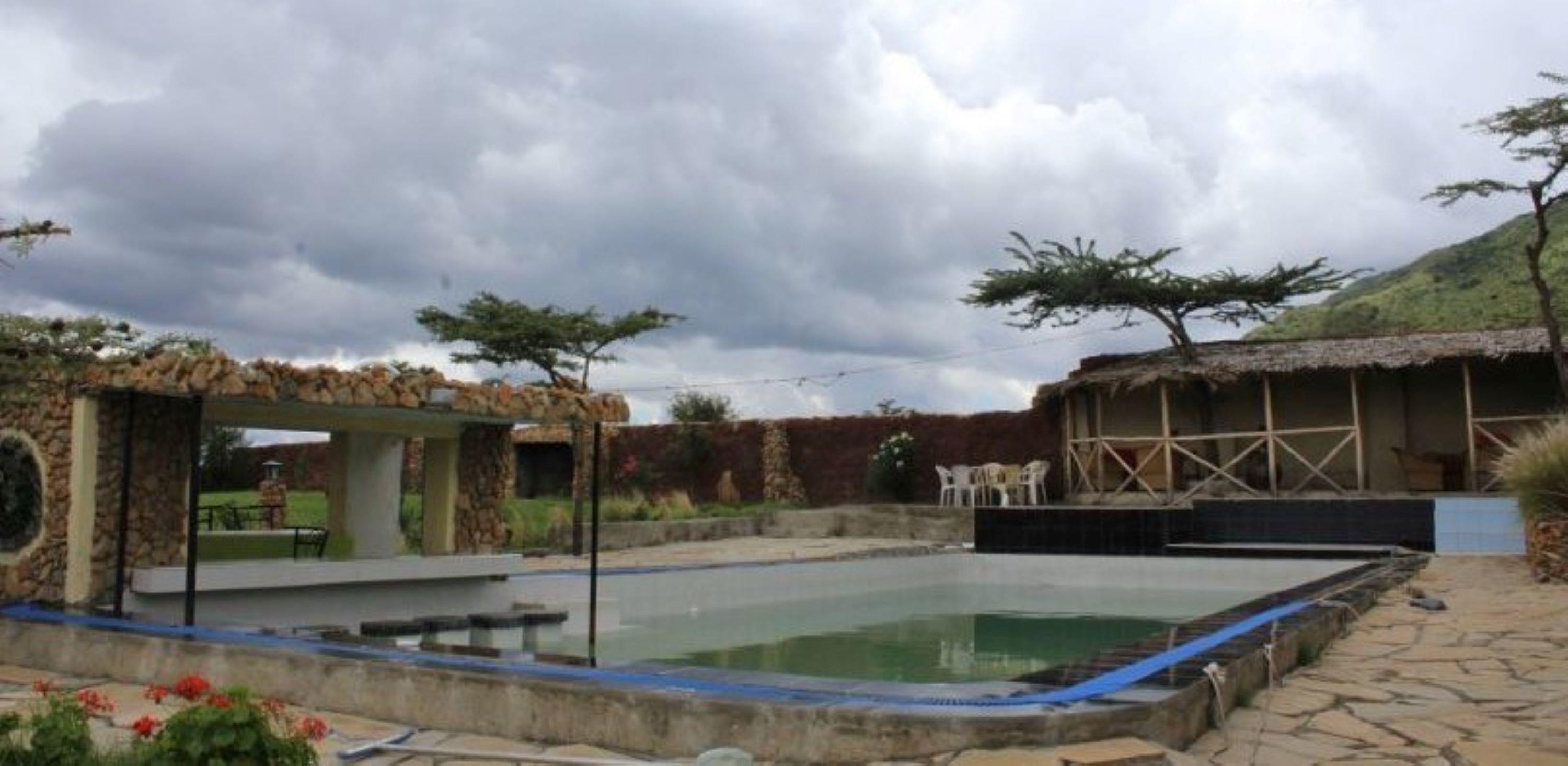 A swimming pool with a stone deck, a covered seating area, and a thatched-roof structure.
