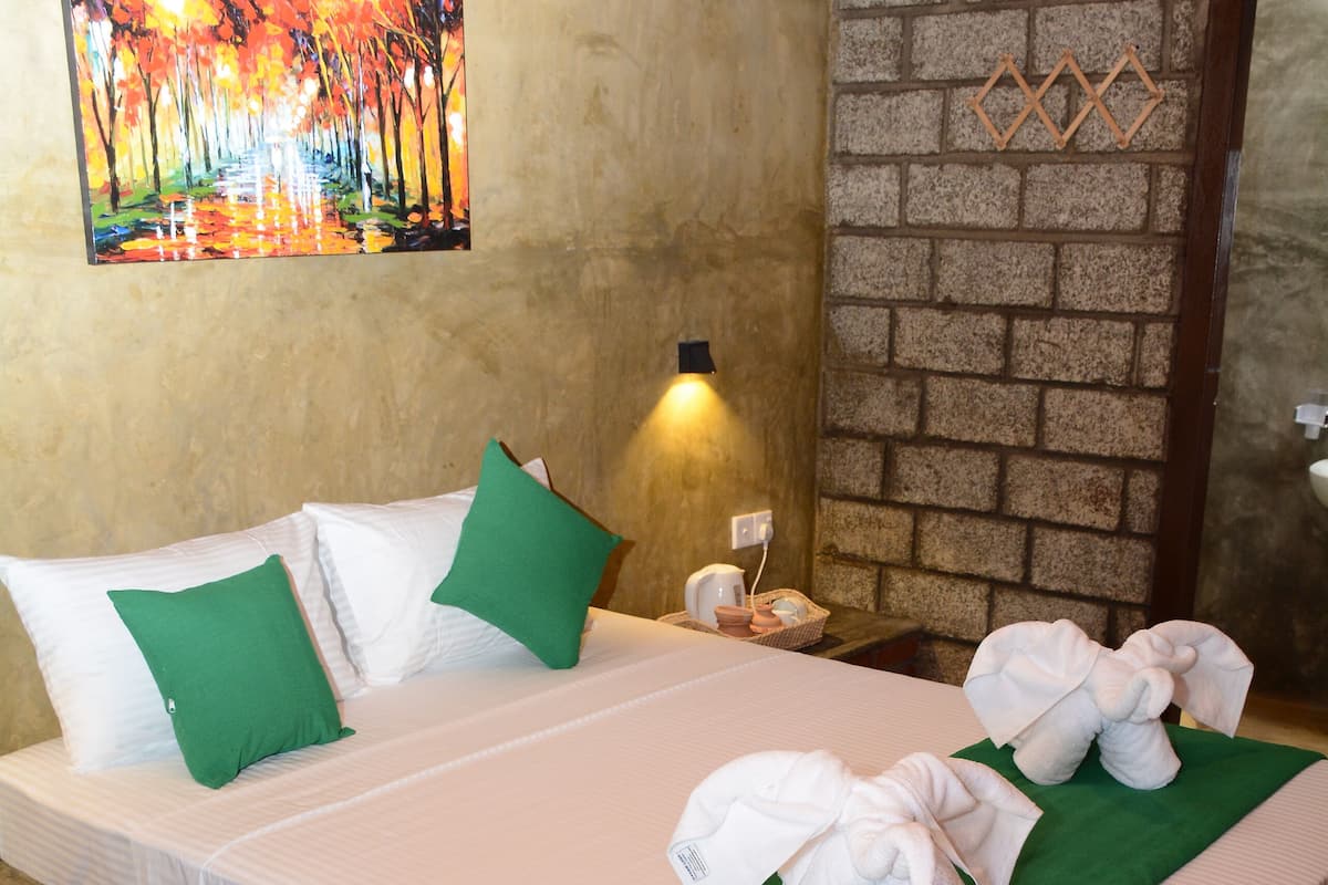 A neatly made bed with green pillows, a green throw blanket, and white towels arranged on the bed.