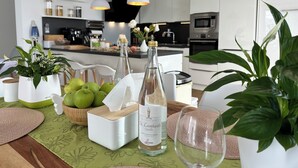 Een moderne keuken met witte kasten, een centraal eiland, hangende pendantlampen en een eetgedeelte met een gedekte tafel voor twee personen.