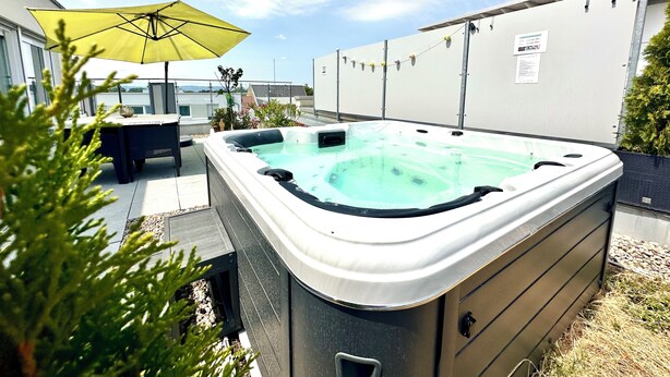 Een jacuzzi met een tafel en stoelen, omringd door potplanten en een gele parasol.