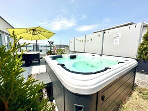 Ein Whirlpool mit Tisch und Stühlen, umgeben von Topfpflanzen und einem gelben Sonnenschirm.