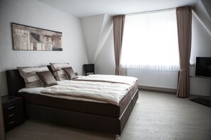 Una camera da letto moderna con un letto grande, comodini, una TV a schermo piatto e una finestra con tende.