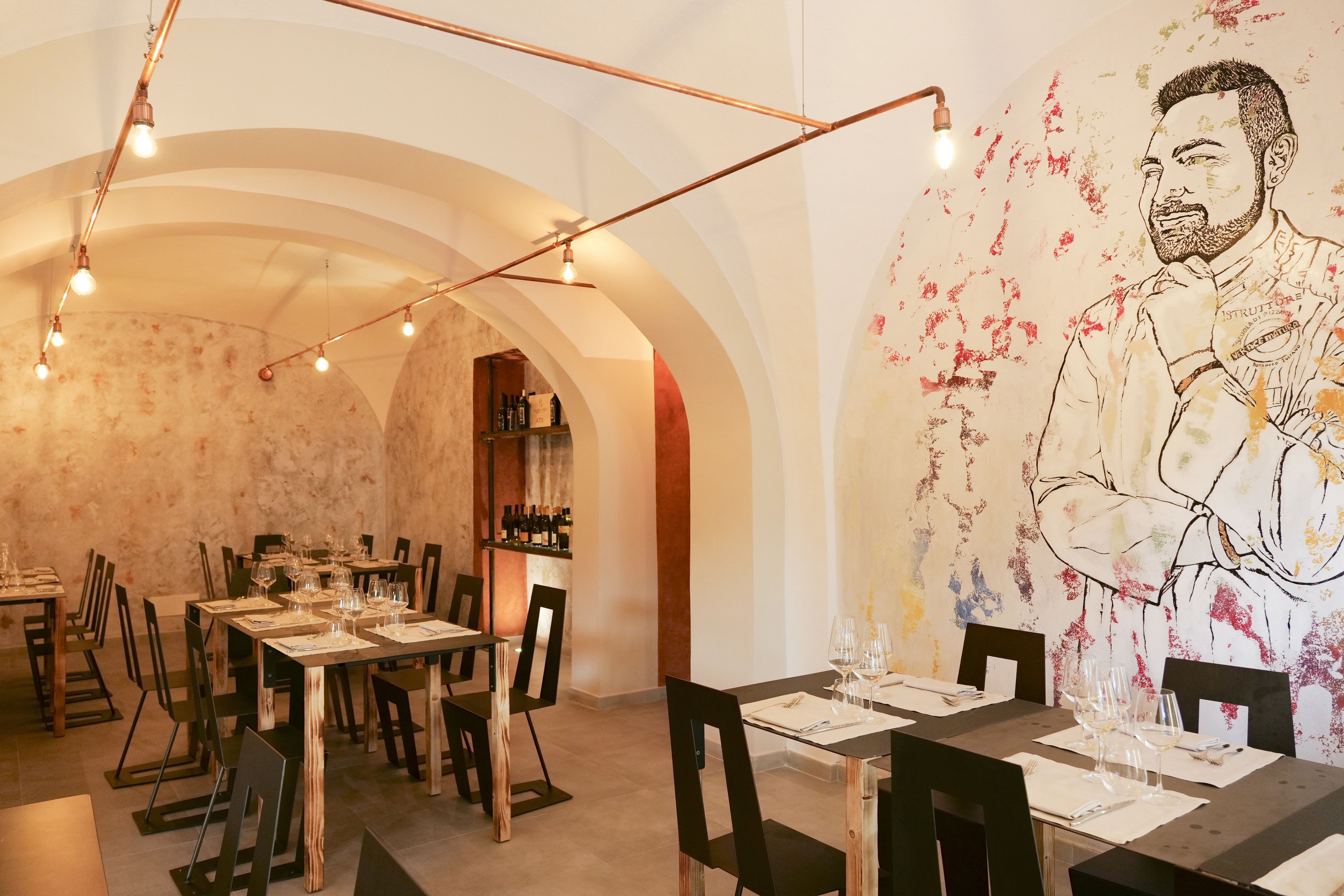 Un comedor con mesas dispuestas para una comida, una estantería para vinos al fondo y un mural en la pared.