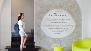 A person standing on a staircase in a modern interior with a wall-mounted text panel and a bright yellow chair. - Hotel La Smorfia (Rosignano Marittimo)