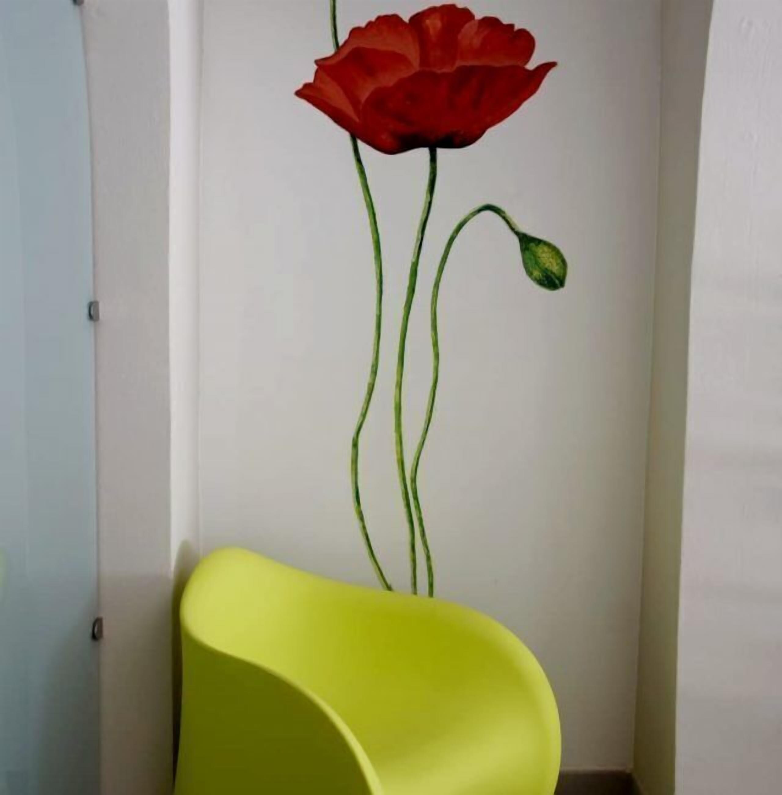 A room with a wall mural of a red poppy and a bright yellow chair.
