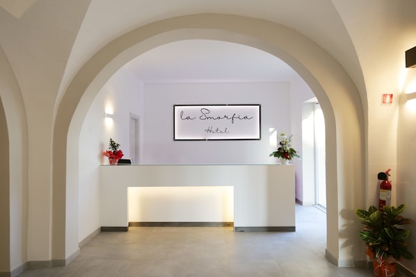 A hotel reception area with a modern design, featuring a reception desk, a framed sign above it, and a fire extinguisher on the wall.